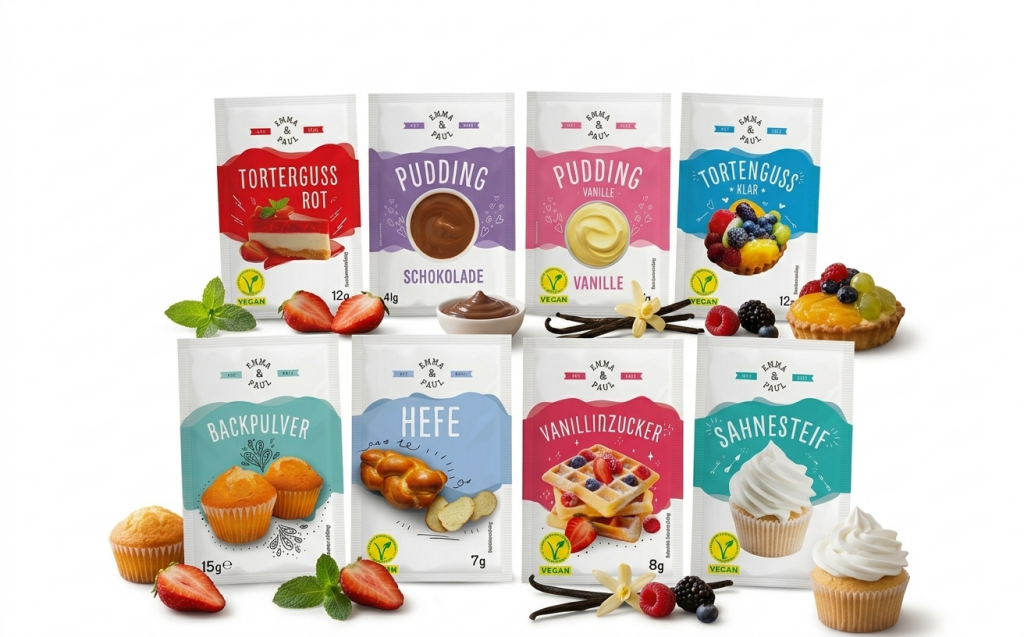 „Acht verschiedene Backzutat-Päckchen der Marke ‚Emma & Paul‘, angeordnet in zwei Reihen auf weißem Hintergrund. Die farbenfrohen Verpackungen (u.a. Pudding, Backpulver, Hefe) sind mit passenden Gebäckstücken wie Muffins, Waffeln und Obsttörtchen sowie frischen Erdbeeren und Vanilleschoten dekoriert.“